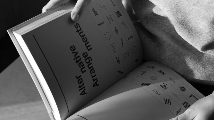 Person holding a book showcasing alternative logotype arrangements